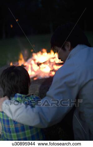 Picture - Father and Son Talking nearby Camp Fire. Fotosearch