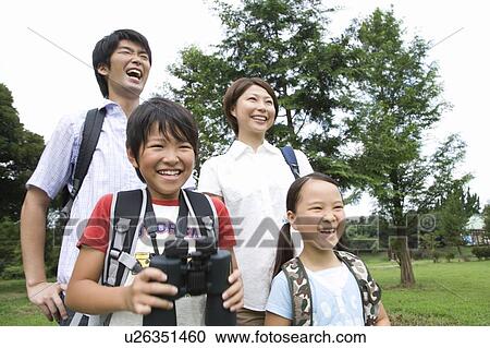 Stock Image - Happy family standing in field, boy holding binoculars. Fotosearch