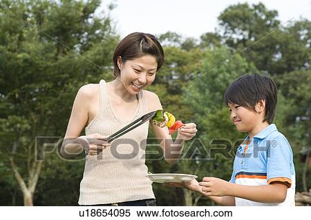 Stock Photography - Mother Holding Grilled Vegetables and Giving it to Son. Fotosearch
