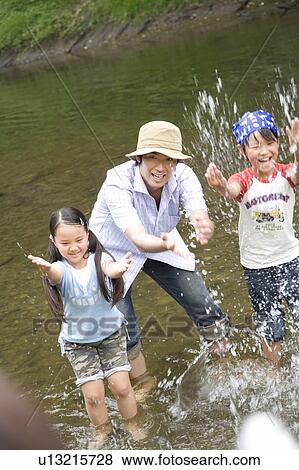 Stock Photo - Two children splashing water in the stream with father, differential focus. Fotosearch
