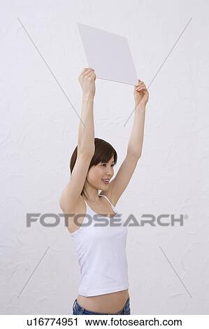 Stock Image - Young woman holding a white board, smiling, side view. Fotosearch