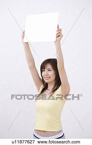 Stock Photo - Young woman holding a white board, smiling, side view. Fotosearch