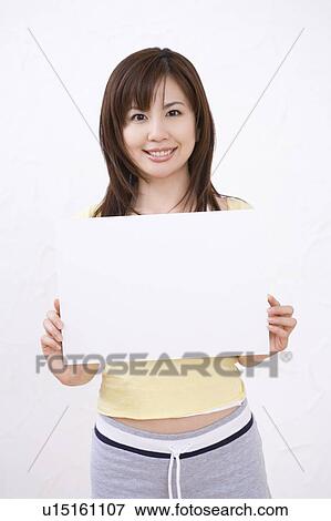 Stock Photo - Young woman holding a white board, smiling, front view. Fotosearch