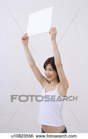 Stock Photograph - Young woman holding a white board, smiling, side view. Fotosearch
