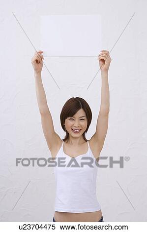 Stock Photography - Young woman holding a white board, smiling, front view. Fotosearch