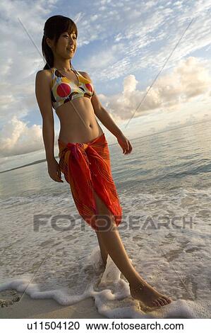 Stock Image - Young woman walking on beach, smiling, Saipan, USA . Fotosearch