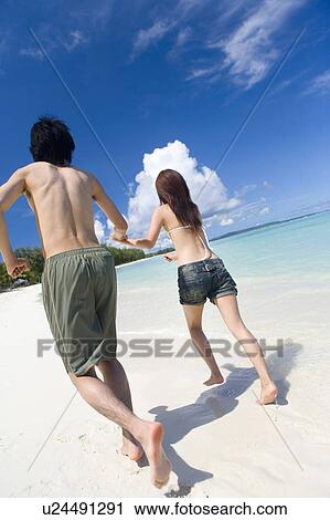 Stock Image - Young couple running on beach, Saipan, USA . Fotosearch