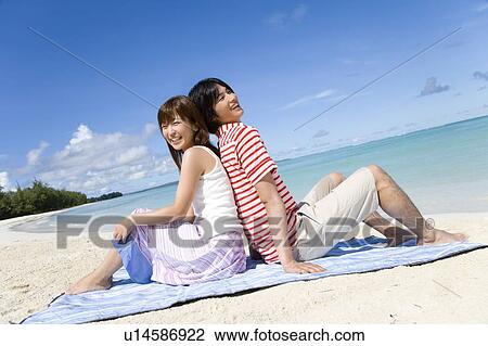 Stock Image - Young couple sitting on beach, back to back, Saipan, USA . Fotosearch