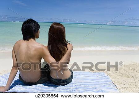 Young couple sitting on beach, man putting arm around woman's shoulders, Saipan, USA View Large Photo Image Picture - Young couple sitting on beach, man putting arm around woman's shoulders, Saipan, USA . Fotosearch