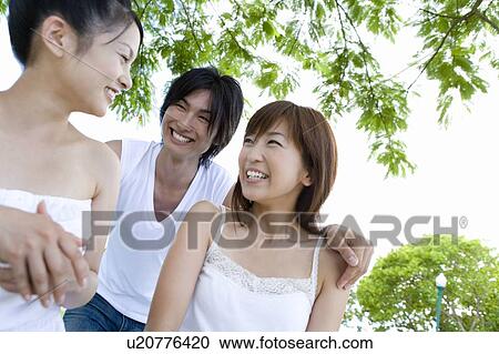 Stock Image - Three young people smiling, man putting hands on women's shoulders, Saipan, USA . Fotosearch