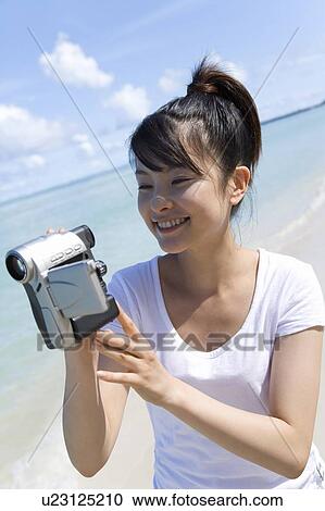 Young woman holding video camera on beach, smiling, Saipan, USA View Large Photo Image Stock Image - Young woman holding video camera on beach, smiling, Saipan, USA . Fotosearch