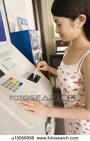 Stock Photo - Young woman using ATM machine, Saipan. Fotosearch