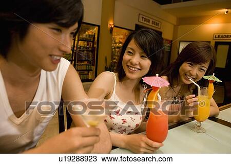 Stock Image - Friends drinking cocktail, Saipan, Focus on Background. Fotosearch