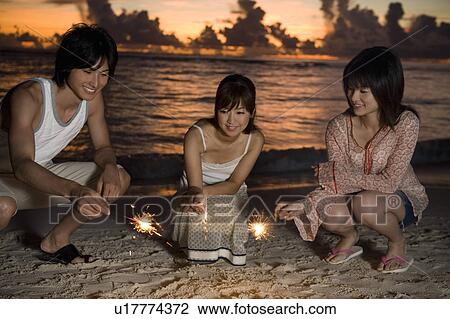 Three young people holding lighting fireworks on beach, long exposure, Saipan, USA View Large Photo Image Stock Image - Three young people holding lighting fireworks on beach, long exposure, Saipan, USA . Fotosearch