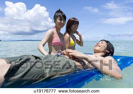 Stock Photo - Three young people in the sea, man lying on a pool raft, Saipan, USA . Fotosearch