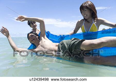 Stock Photo - Three young people playing in the sea, smiling, Saipan, USA . Fotosearch