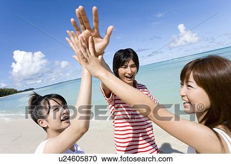 Stock Image - Three young people smiling and giving high fives on beach, Saipan, USA . Fotosearch