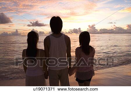 Stock Image - Three young people standing on beach in the evening, Saipan, USA . Fotosearch