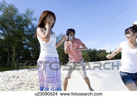 Picture - Young man filming women on beach, Saipan, USA . Fotosearch