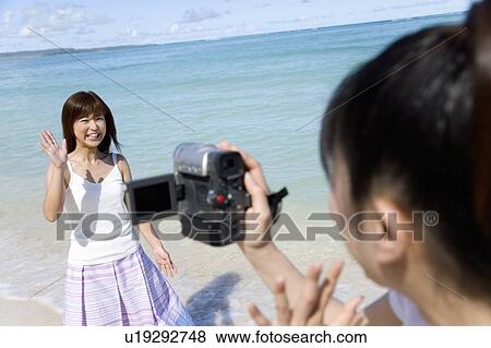 Stock Photo - Young woman filming friend on beach, waving hands, Saipan, USA . Fotosearch