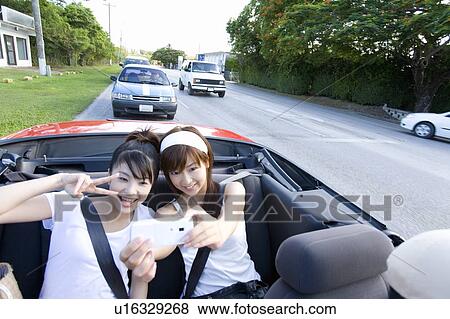 Stock Photo - Young women taking picture of themselves in car, Saipan, USA . Fotosearch