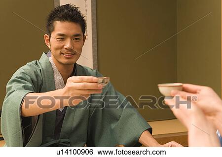 Stock Photograph - Japanese couple in Yukata holding up Sake cups, front view, Japan. Fotosearch