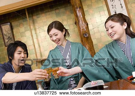 Stock Photography - Three young people toasting with glasses, front view, Japan. Fotosearch