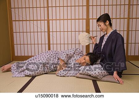 Stock Photo - Woman fanning man, resting his head on her lap in the room, front view, side view, Japan. Fotosearch