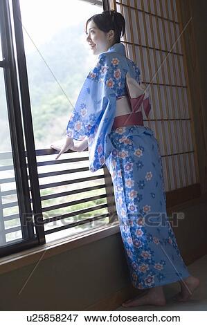 Stock Photo - Woman in Yukata looking outside from the window, side view, Japan. Fotosearch
