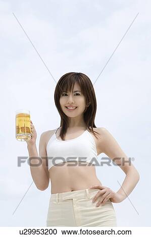 Stock Image - Young woman holding a beer glass, low angle view. Fotosearch