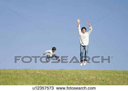 Stock Image - Father and son jumping on grass. Fotosearch
