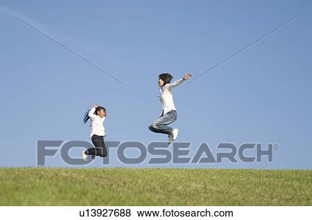 Stock Photo - Mother and daughter jumping on grass. Fotosearch