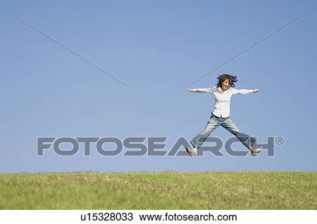 Stock Image - Young woman jumping on grass. Fotosearch