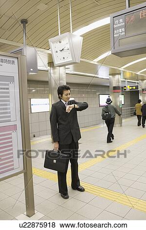 Stock Photo - Businessman looking at wristwatch at station. Fotosearch