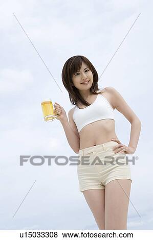 Stock Photo - Young woman holding a beer glass, low angle view. Fotosearch