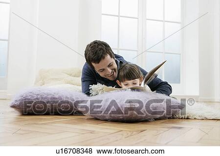 Stock Photo - Father and daughter reading book on floor, low angle view. Fotosearch