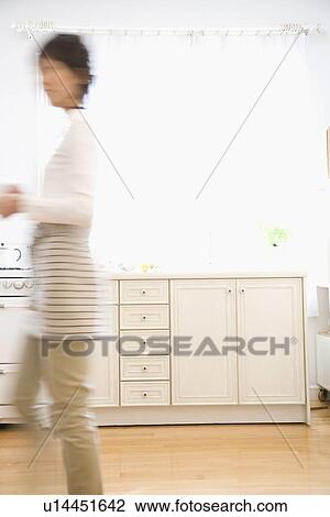 Stock Image - Young woman walking in kitchen. Fotosearch