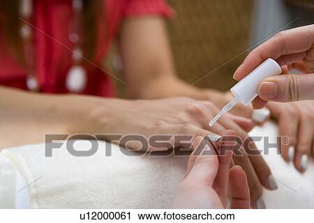 Stock Image - Young woman applying manicure at nail salon. Fotosearch