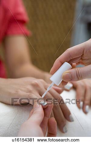 Stock Image - Young woman applying manicure at nail salon. Fotosearch