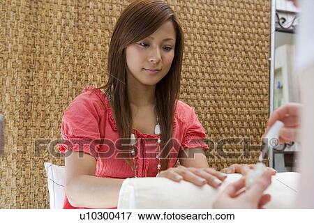 Stock Photo - Young woman applying manicure at nail salon. Fotosearch