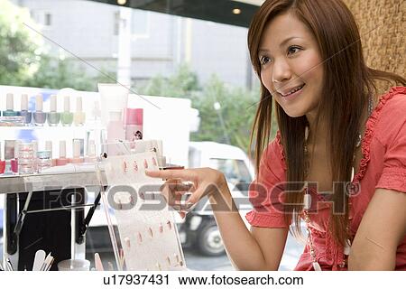 Stock Image - Young woman choosing artificial nails. Fotosearch