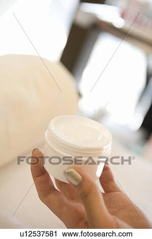 Stock Image - Young woman opening moisturizer. Fotosearch