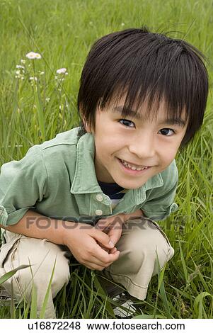 Stock Photo - Boy crouching on grass field. Fotosearch