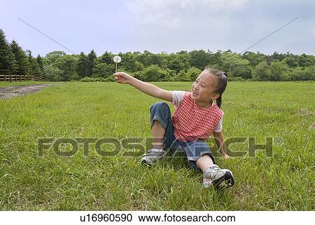 Stock Image - Girl holding dandelion seeds. Fotosearch