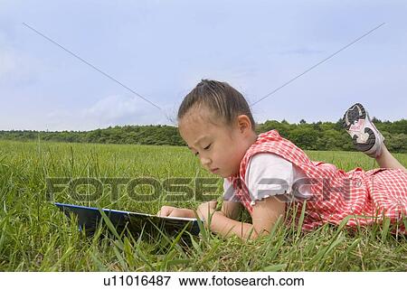 Stock Photo - Girl reading book on grass field. Fotosearch