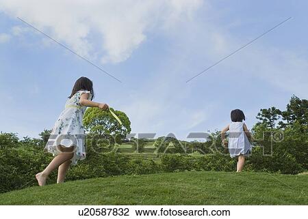 Stock Image - Two girls running on grass field. Fotosearch
