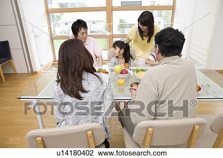 Stock Image - Family sitting at dining table. Fotosearch