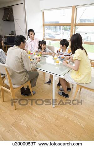 Stock Photo - Family sitting at dining table. Fotosearch