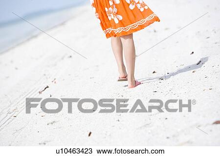 Stock Image - Legs of young woman walking at beach. Fotosearch