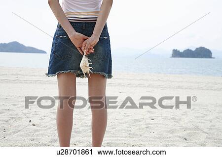 Stock Image - Rear view of young woman holding seashell. Fotosearch